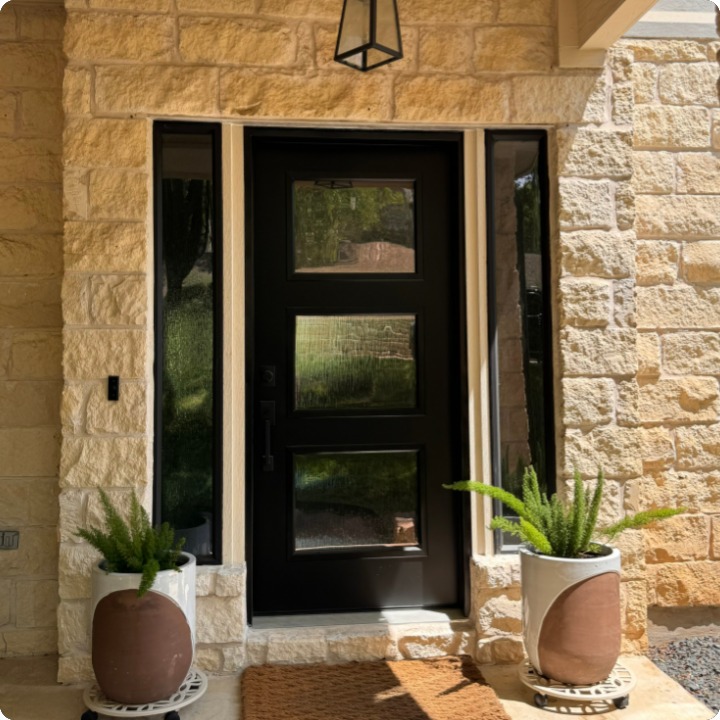 Black three-lite modern entry door with sidelites on a stone home
